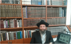 Reb Eliyahu Sitting by His Computer with His Torah Library in the Background